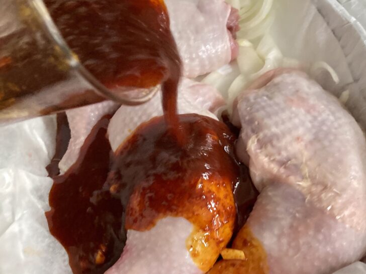 baked chicken with potatoes - the chicken is lying in the pan, on the onion rings, and on top, the sauce is being poured all over.