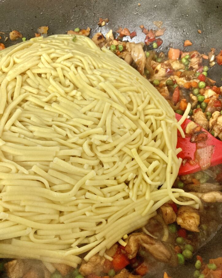 Adding Lo Mein Noodles to chicken-veggie mixture frying in wok