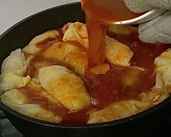 Pouring sauce over cabbage rolls in pot, before cooking