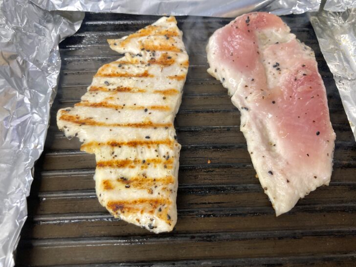 The first Chicken breast cutlet on a hot griddle has been flipped over. The cutlet on the right is ready for flipping. Its edges are white while the center is pinkish.